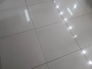 Obraz premium Glossy white ceramic floor tiles texture with bright ceiling light reflections and dark diagonal grout lines.