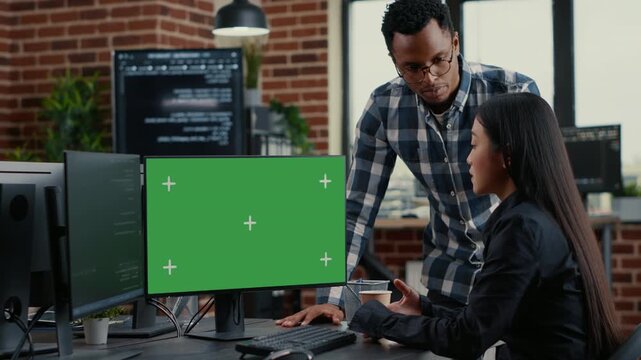 Mixed software development team analyzes source code near a green screen chroma key mockup, combining team debugging, screen replacement and software collaboration
