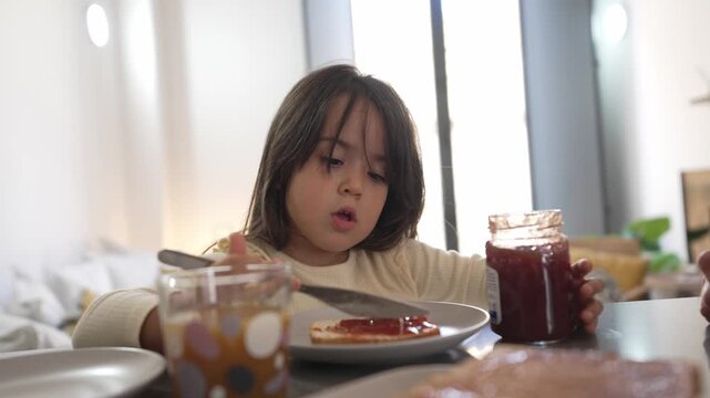 Adorable little girl spreading jam on toast