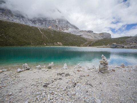 Stones arranged on rocky shore by Milk Lake in Sichuan with turquoise water and mountains in the background on Tibetan Plateau