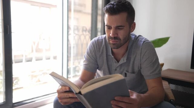 Concentrated handsome man reading book near window