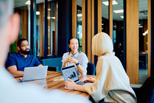 Diverse team of professionals discussing data and strategy while working together on laptops during a corporate gathering