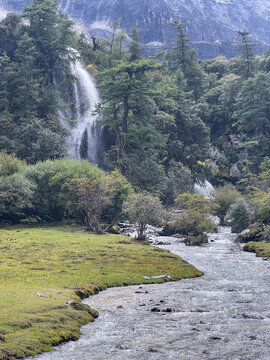 Waterfall and river flow through Luorong Pasture in Yading Nature Reserve,Daocheng, Sichuan, China with lush meadows and forests