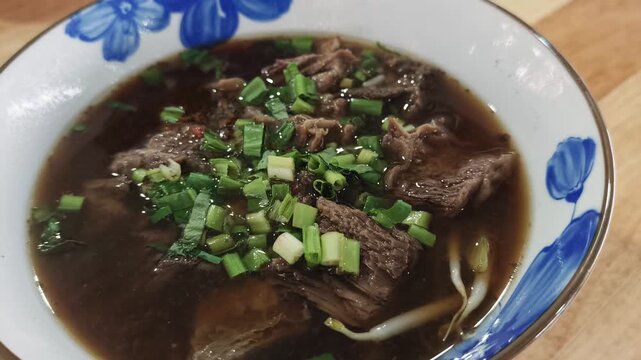 Thai Beef Boat Noodle Soup with Fresh Herbs in Bowl, Traditional Street Food, Close Up Video