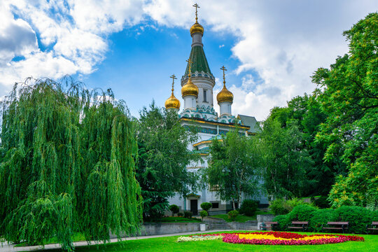 Golden domes of Saint Nicholas The Miracle Maker Russian Church stand out in Sofia's greenery on a bright day