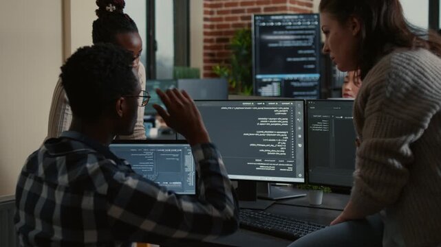 Software development team analyzes a coding project together, using laptop and monitor displays to coordinate software development tasks, while debugging software errors.