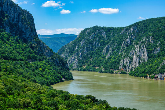 Danube river flows through steep mountains at Iron Gates gorge in Serbia with Romania across the water on a sunny day