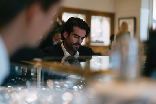 A charismatic man in a tailored suit carefully considers his options while admiring exquisite jewelry, embodying confidence, taste, and an eye for luxury in a fine retail atmosphere.