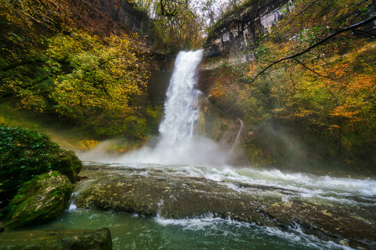 Sugarloaf waterfall cascades over rocks surrounded by colorful autumn trees in France near Surjoux