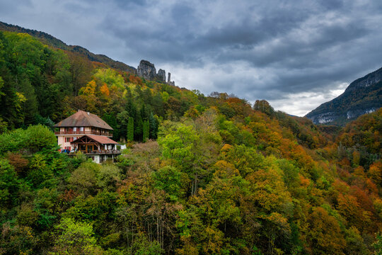 House rests on a mountainside surrounded by forest and autumn colors under a cloudy sky in France