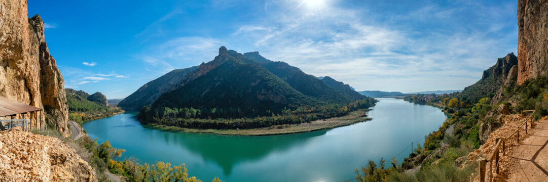 Panorama of Sant Llorenc de Montgai reservoir reflecting sunlight amidst green mountains under blue sky in Spain