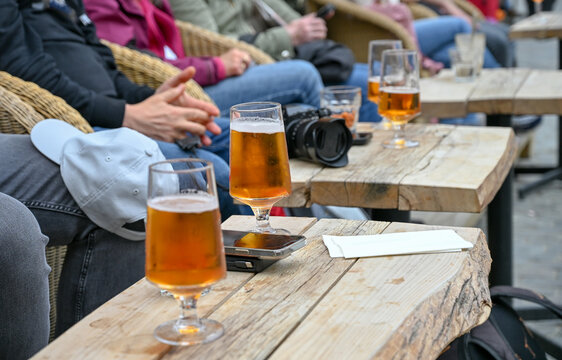 People enjoying cold beer on an outdoor caf&eacute; terrace. Friends drinking refreshing beer on a wooden patio. Cold draft beer served on a table in restaurant.