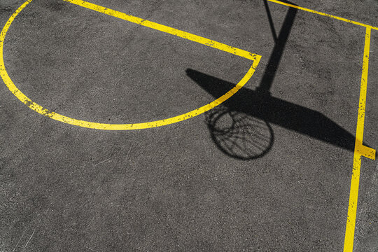 A cinematic basketball hoop casting a shadow on rough asphalt&mdash;ideal for editorial or advertising purposes. It evokes the feeling of streetball on a sunny day.