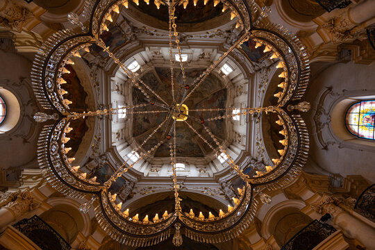 Baroque chandelier hangs under ornate dome ceiling in St. Nicholas Church with detailed artwork and glass windows in a historic setting