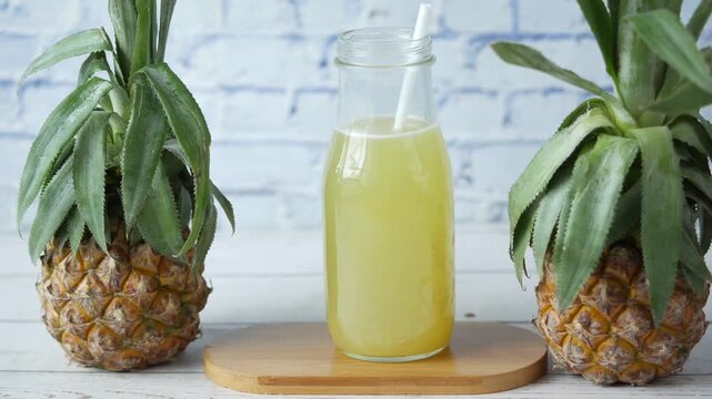 Fresh pineapple juice in glass bottle with straw on white table against brick wall background