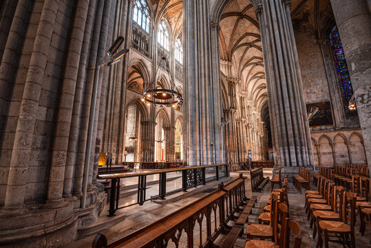 Exploring the side aisle of Rouen Cathedral with tall columns, ribbed vaults, and stained glass showing light