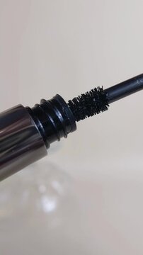 Opening mascara product cap and removing the black wand brush from inside silver tube packaging. Beauty tool, eye makeup application process.