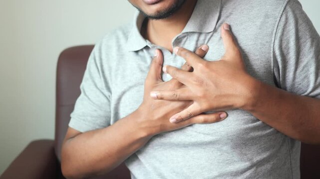 Young man experiencing sudden chest pain while sitting on sofa at home indoors
