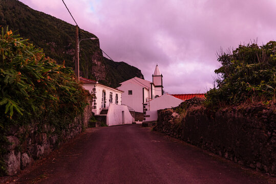 Rural road leads towards Igreja de Nossa Senhora do Carmo on Flores Island in Portugal with cliffs in the background