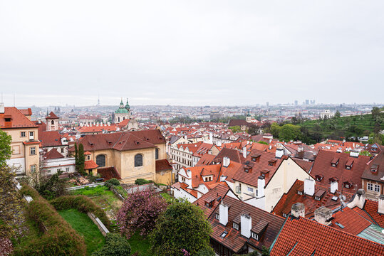 Rooftops of Mal Strana in Prague show old buildings, red-tile roofs, and greenery under a cloudy sky