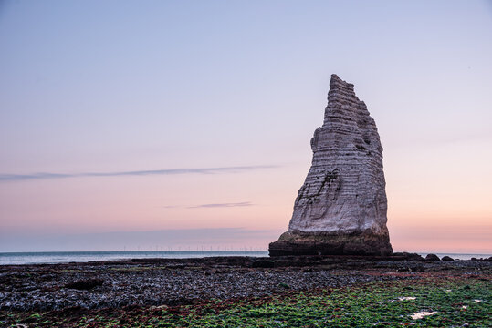 Distinctive Aiguille d'Etretat sea stack stands at dusk on the Normandy coastline in France illuminated by soft light