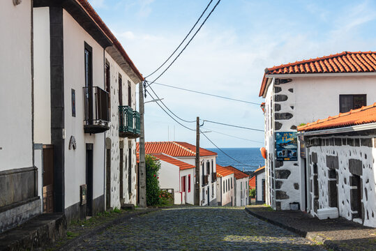 Narrow cobblestone street with white houses in a coastal village on Flores Island in Portugal