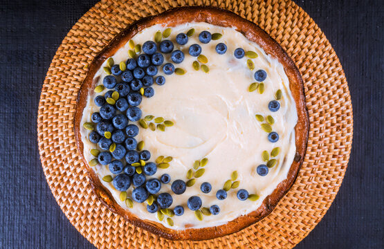 Fresh cake with blueberries, seeds on woven plate at kitchen table