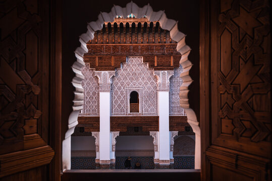 View through carved cedarwood arch into Ben Youssef Madrasa courtyard showing Moorish geometry and craftsmanship in Marrakesh, Morocco