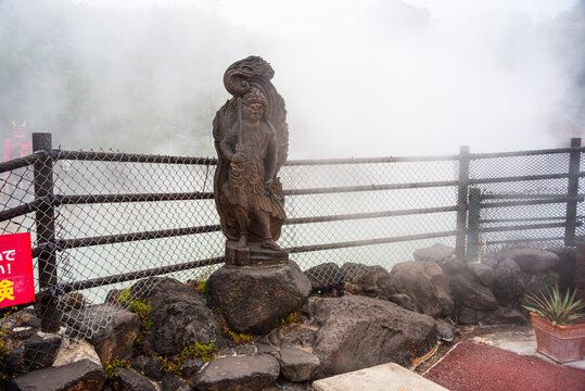 Stone statue of a guardian deity standing at a geothermal site in Japan&rsquo;s hot spring region, representing local culture and nature's power