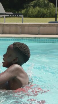 Vertical video: Dad carrying son in red trunks on shoulders, playing in home pool by beach ball