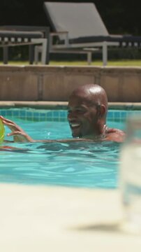 Vertical video: Holding green float, shirtless dad playing with teen at pool, swimming toward glass