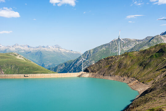 View across Griessee and its dam with alpine slopes and wind turbines in Switzerland