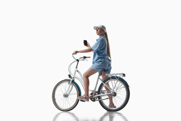 Fototapeta premium Woman sitting on bicycle and holding smartphone on white background. Concept of bike navigation app, urban delivery service, mobile route planning and bicycle rental promotion.
