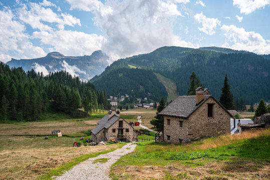 Stone houses stand in alpine pasture under cloudy skies near larch forests in Italy's high mountains