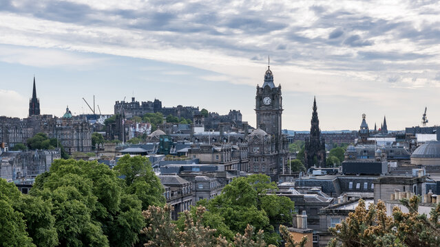 View of Edinburgh skyline from Calton Hill showing iconic landmarks and green trees under a soft sky
