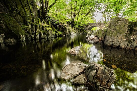 River Esk flows under Trough House Bridge on a sunny day with passing showers in Eskdale, UK