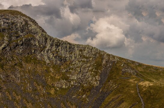Hikers walk along Sharp Edge with Blencathra peak in the background on a cloudy day in the Lake District