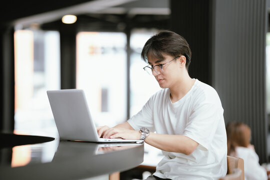Young professional talking on smartphone while working on a laptop in a modern caf&eacute;, holding a coffee cup with natural window light.