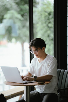 Young professional talking on smartphone while working on a laptop in a modern caf&eacute;, holding a coffee cup with natural window light.