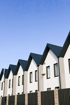 Row of modern white houses with dark roofs under a clear blue sky