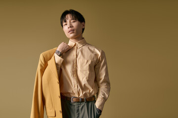 Fototapeta premium A young Asian man exudes charm in fashionable clothing while posing confidently.