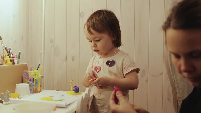 Mother and little daughter creating colorful modeling clay figures together in her own room