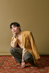 Fototapeta premium A handsome young Asian man squats thoughtfully in chic clothing, showcasing modern style and flair.