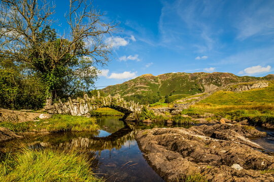 Scene of Slaters Bridge and the surrounding landscape in Little Langdale Valley under blue sky in Lake District Cumbria