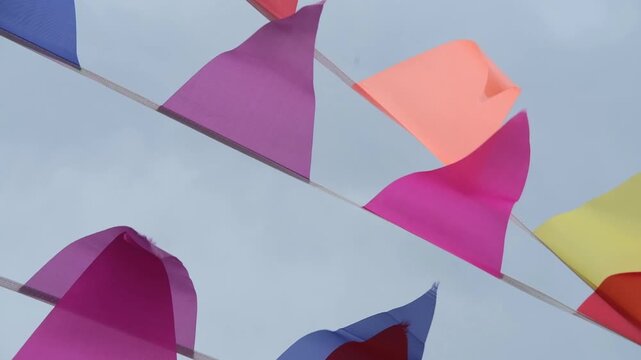 Colorful fabric flags fluttering in the wind against a cloudy sky, showcasing vibrant hues of pink, orange, yellow, and blue in a festive outdoor setting