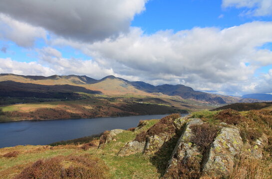 View across Coniston Water towards Coniston mountain range with clouds in the sky and rocks in the foreground in the UK