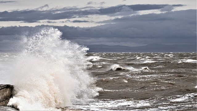 Breezy day with ocean waves crashing on the coast in Barrow In Furness, with view towards Morecambe Bay in the United Kingdom