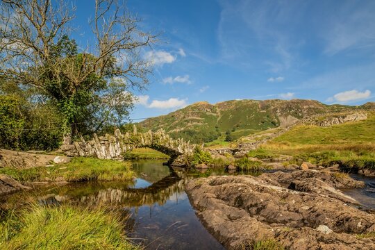 Historic slate packhorse bridge in Little Langdale Valley features unique design with natural boulder and slate near water