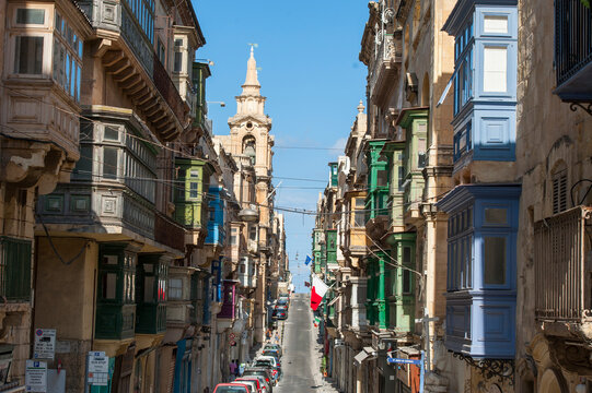 Walking along St.Paul street with colorful balconies and a church tower in Valletta, Malta