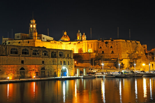 Night view of port with boats and historic buildings in Senglea, Malta, showcasing the lights along the waterfront